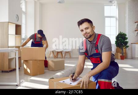 Moving service workers pack cardboard boxes and checking list in client's apartment. Stock Photo