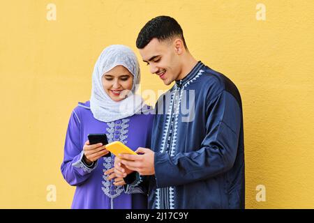 Happy young couple using smart phone in front of yellow wall Stock Photo