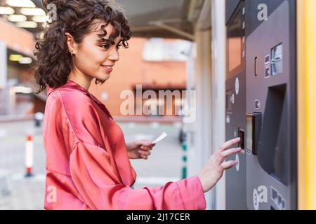 Young woman buying ticket from machine at station Stock Photo