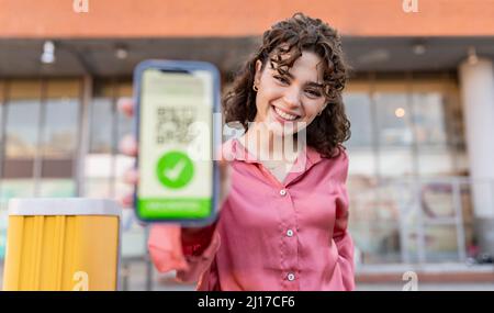 Smiling woman showing QR code over smart phone Stock Photo