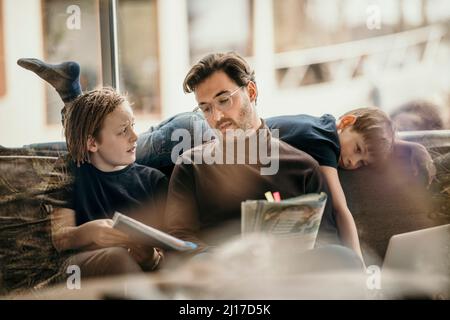 Man explaining to son with boy lying on sofa at home Stock Photo