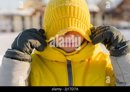 Boy covering eyes with yellow knit hat in winter Stock Photo