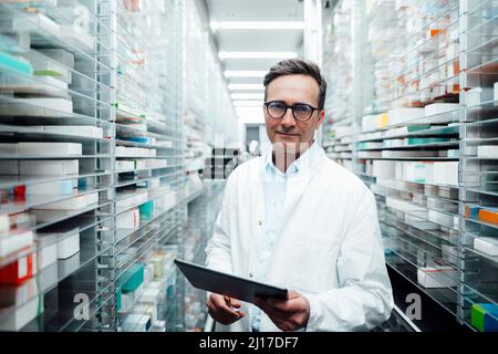 Pharmacist with tablet PC standing in storage room at pharmacy Stock Photo