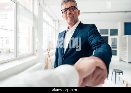 Smiling businessman shaking hand with colleague in office Stock Photo