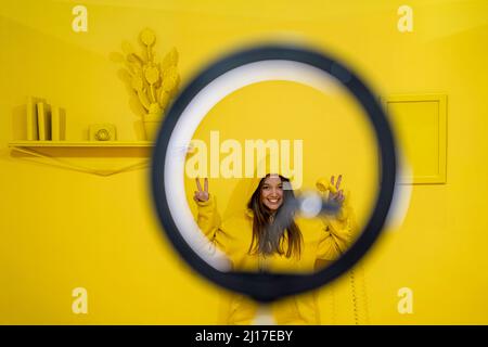 Happy woman smiling through ring light against yellow background Stock Photo