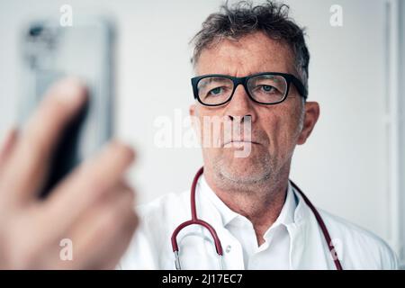Serious doctor using smart phone in front of wall Stock Photo