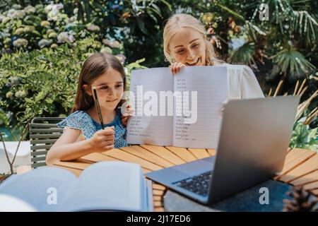 Daughter and mother showing homework on video call over laptop Stock Photo
