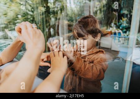 Boy gesturing to mother and sister through window Stock Photo