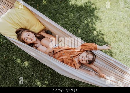 Smiling sister and brother lying in hammock at back yard Stock Photo