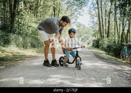 Father teaching son to ride cycle on road Stock Photo