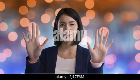 Portrait of asian businesswoman touching invisible screen against spots of light in background Stock Photo