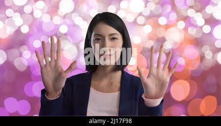 Portrait of asian businesswoman touching invisible screen against spots of light in background Stock Photo