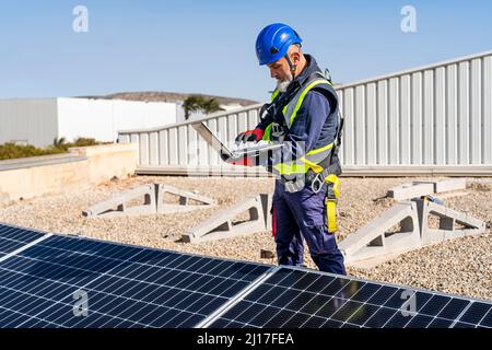 Technician working on laptop by solar panels at solar power station Stock Photo