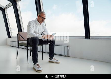 Businessman text messaging on mobile phone in startup office Stock Photo