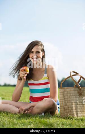 Happy woman with apple sitting in grass on meadow Stock Photo