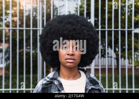 Serious woman with afro hairstyle in front of fence Stock Photo