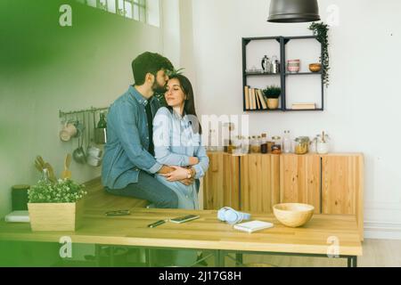 Man kissing on girlfriend's forehead in kitchen Stock Photo