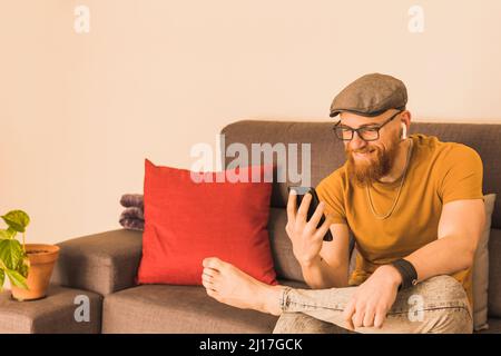 Bearded man having video call on smart phone sitting in living room Stock Photo