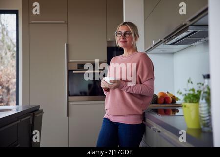 Blond woman holding coffee cup standing in kitchen Stock Photo