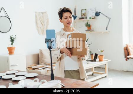 Influencer with packages vlogging in front of smart phone at workshop Stock Photo