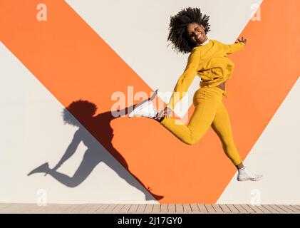 Happy woman jumping by wall on sunny day Stock Photo