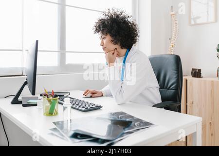 Doctor sitting with hand on chin using computer at medical clinic Stock Photo