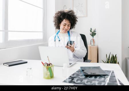 Doctor sitting with laptop using mobile phone at medical clinic Stock Photo