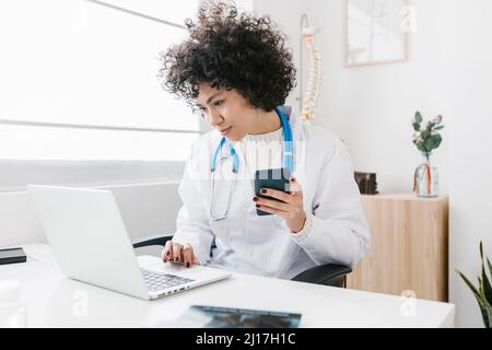 Young doctor holding smart phone using laptop at clinic Stock Photo