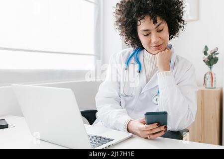 Doctor sitting with laptop using mobile phone at clinic Stock Photo