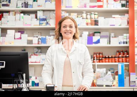 Happy female pharmacist standing at checkout counter in pharmacy store Stock Photo