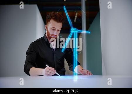 Engineer working on digital display by wind turbine at desk in office Stock Photo