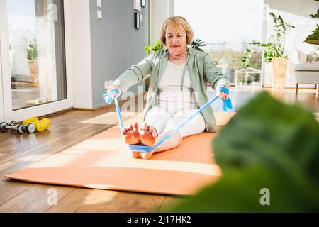 Senior woman exercising with resistance band at home Stock Photo
