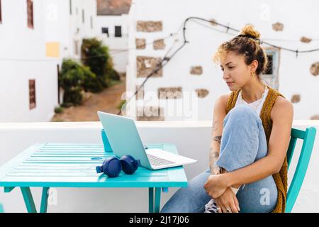 Young woman with laptop sitting at table on rooftop Stock Photo