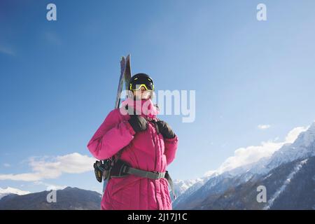 Man wearing warm clothing carrying skis in winter Stock Photo