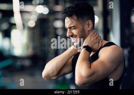 Body Injury. Portrait of young arab man suffering from pain in neck Stock Photo
