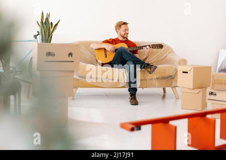 Young man practicing guitar sitting on sofa at home Stock Photo