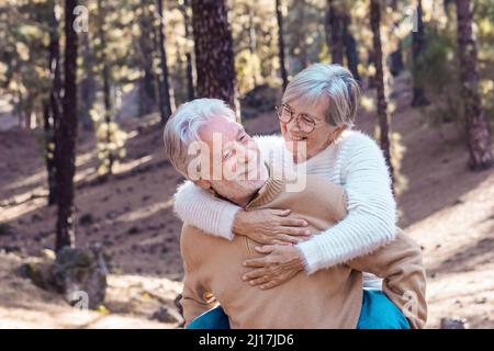 Happy senior man giving piggyback ride to woman in forest Stock Photo