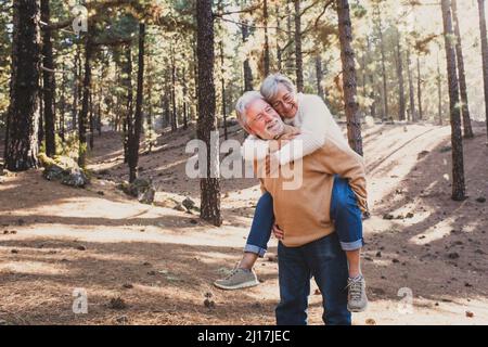 Smiling senior man giving piggyback ride to woman in forest Stock Photo