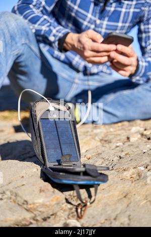 Man charging mobile phone through portable solar panel on sunny day Stock Photo