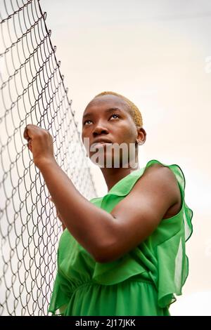 Young woman with short blond hair by chainlink fence Stock Photo