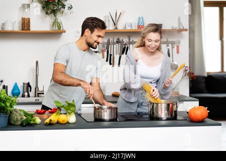 Smiling young man looking at girlfriend making pasta in kitchen Stock Photo