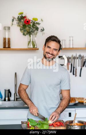 Happy young man chopping food standing in kitchen at home Stock Photo