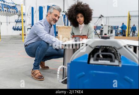 Engineer in squatting position discussing with developer in factory Stock Photo