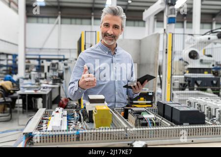 Smiling engineer holding tablet PC standing by machine in factory Stock Photo