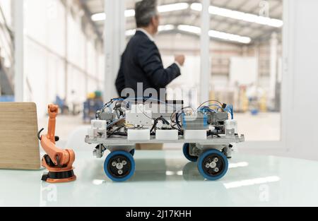 Model of robotic arm and vehicle on desk with businessman standing in background at factory Stock Photo