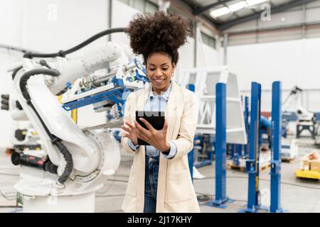 Smiling businesswoman using tablet PC standing in factory Stock Photo