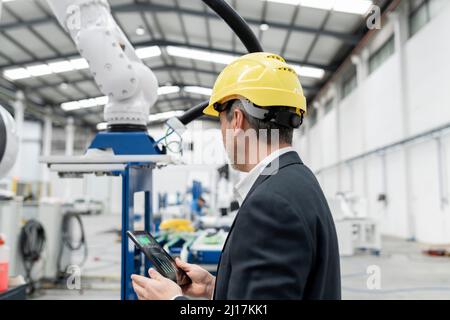 Engineer examining robotic arm through tablet PC in factory Stock Photo