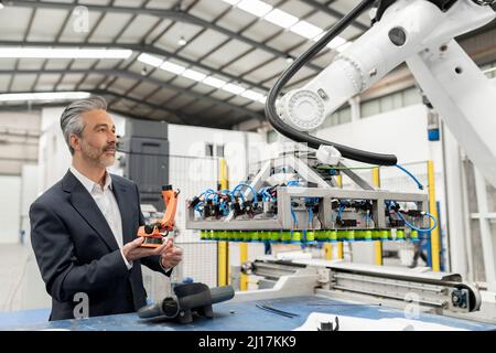Businessman holding robotic arm model examining machinery in factory Stock Photo