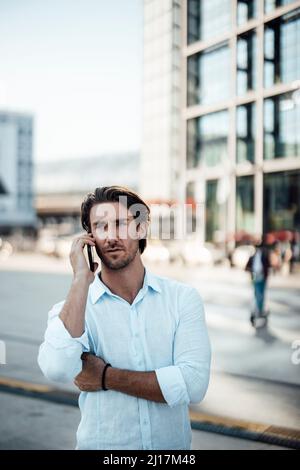 Handsome businessman talking on smart phone at footpath Stock Photo
