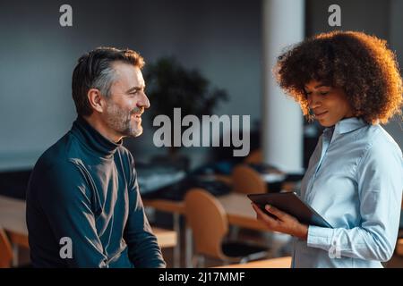 Happy businessman discussing with colleague using tablet PC at work place Stock Photo